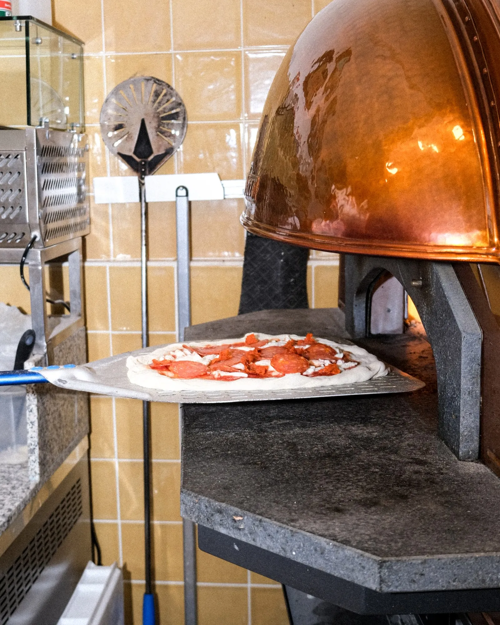 A pizza going into the glowing copper gas oven at Filomena, the Neapolitan pizzeria in Larnaca, Cyprus